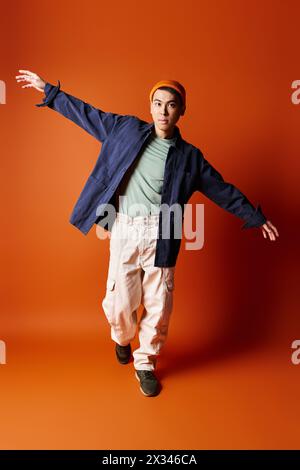 Ein hübscher asiatischer Mann in blauer Jacke und khakifarbener Hose posiert vor einem orangen Hintergrund in einem Studio-Setting. Stockfoto