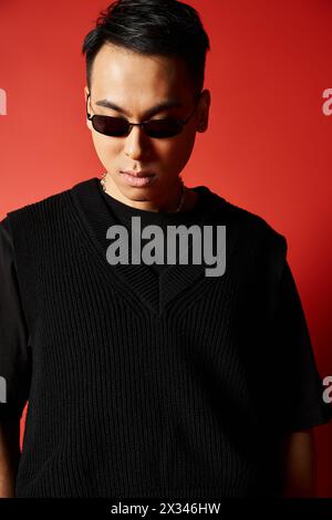 Ein stilvoller und hübscher asiatischer Mann mit Sonnenbrille und schwarzem Pullover vor einem leuchtend roten Hintergrund. Stockfoto