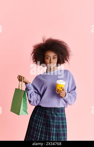 Eine Afroamerikanerin mit lockigen Haaren lächelt, während sie eine Kaffeetasse und einen Papierbeutel hält. Stockfoto