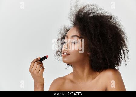 Eine schöne junge afroamerikanische Frau mit lockigem Haar, die Lippenstift aufträgt, in einem Studio-Setting Stockfoto