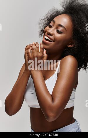 Eine schöne junge afroamerikanische Frau mit lockigem Haar, die ein weißes Top trägt, hell lächelt und in die Hände klatscht. Stockfoto