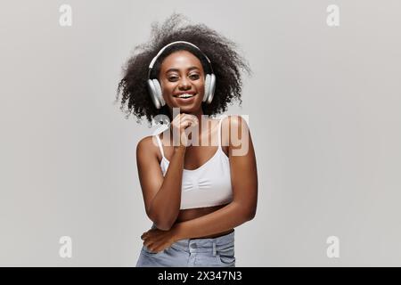 Eine junge afroamerikanische Frau mit lockigen Haaren steht vor weißem Hintergrund und trägt Kopfhörer. Stockfoto