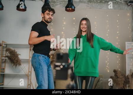 Weißes schönes junges Paar, das Tanzbewegungen mit Smartphone-Kamera im Wohnzimmer aufnimmt. Live-Streaming von Inhalten. Online-Übertragung Stockfoto