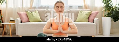 Eine Frau mittleren Alters führt anmutig Yoga vor einer Couch aus. Stockfoto