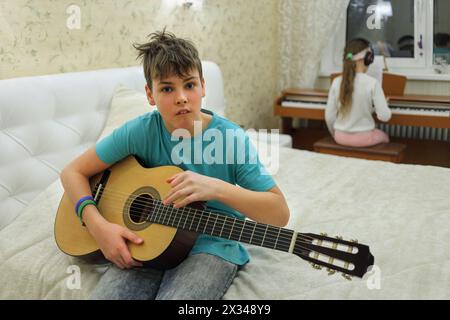 Zwei Personen im Schlafzimmer: Junge mit Gitarrenhalter, das im Hintergrund auf Synthesizer spielt Stockfoto