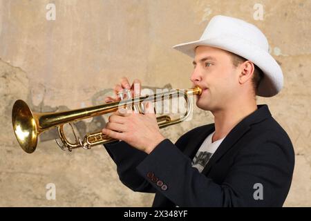 Junger, gutaussehender Mann in weißem Hut und Jacke spielt Trompete im Studio Stockfoto