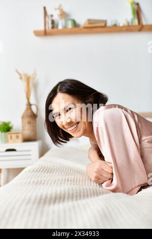 Eine reife Frau in kuscheliger Hauswäsche entspannt sich auf einem weißen Bett. Stockfoto