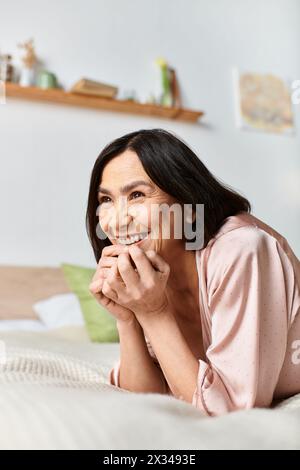 Eine reife Frau in gemütlicher Hauswäsche, die auf einem Bett lächelt. Stockfoto