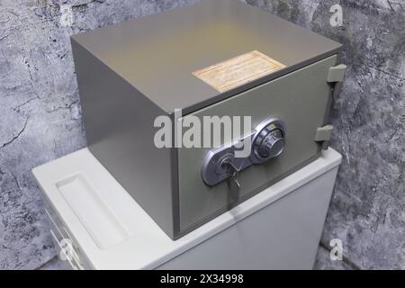 Kleiner Metallsafe mit Schlüssel und Kombinationsschloss in der Ecke des Zimmers Stockfoto