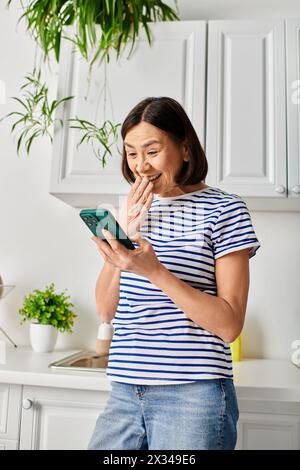 Reife Frau in kuscheliger Hausbekleidung steht in der Küche, hält Tablette. Stockfoto