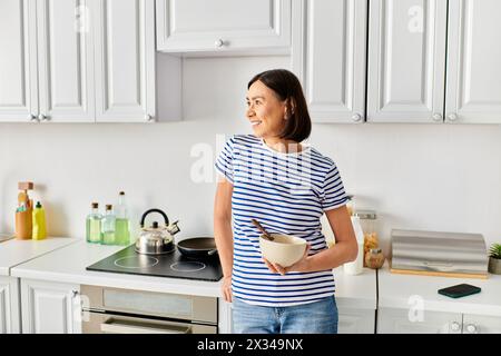 Eine reife Frau in kuscheliger Hauswäsche, die eine Schüssel in ihrer Küche hält. Stockfoto