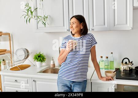 Eine reife Frau in kuscheliger Hauswäsche steht am Waschbecken. Stockfoto