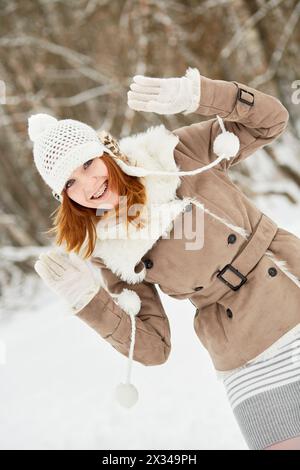 Rothaariges lächelndes Teenager-Mädchen mit Zahnspangen blickt aus der Seite im Winterpark. Stockfoto