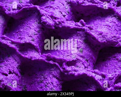 Gefrorenes Eis mit Lavendelgeschmack – Vollformatdetail des Sorbets. Nahaufnahme einer violetten Oberflächenstruktur von Eis gefüllt mit gemischten Blüten. Stockfoto
