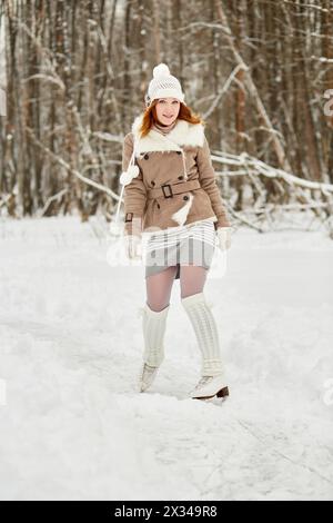 Rothaariges Teenager-Mädchen mit Zahnspangen steht auf Schlittschuhen am Eisweg im Winterpark. Stockfoto