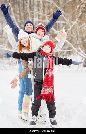 Lächelnde vierköpfige Familie steht auf Schlittschuhen auf dem Eisweg im Winterpark und breitet Arme an die Seiten aus. Stockfoto