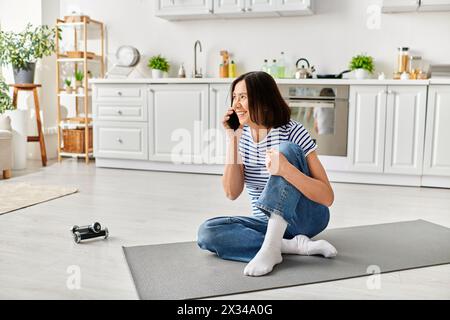 Eine reife Frau in gemütlicher Hausbekleidung sitzt auf dem Boden und führt ein Telefongespräch. Stockfoto