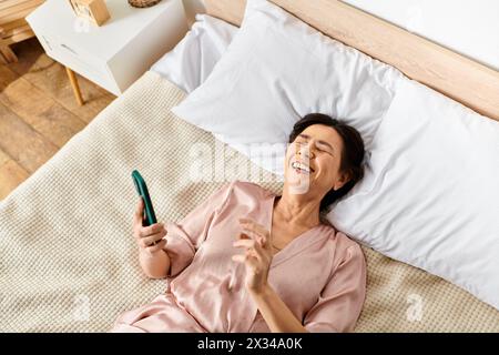 Eine reife Frau in kuscheliger Hauswäsche liegt auf einem Bett und hält eine Zahnbürste. Stockfoto