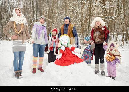 Drei Erwachsene und vier Kinder halten Hände um die gefüllte Maslenitsa im Winterpark. Stockfoto