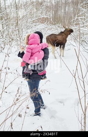 Junger Mann mit Baby in den Armen macht Schnappschuss von Elchfutter im Winterpark. Stockfoto