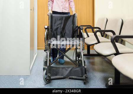 Frau, die sich an Rollstühlen hält, die in der Lobby des Krankenhauses stehen, bereit zum Transport des Patienten Stockfoto