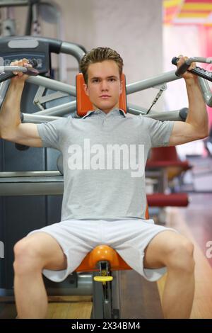 Ein junger Kerl, der sich mit den Händen auf einem Fitnessgerät im Fitnessclub bewegt Stockfoto