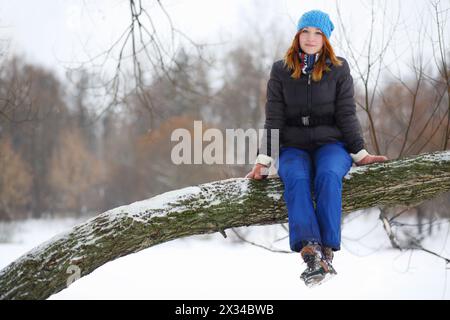 Mädchen Teenager sitzt auf dicken Zweigen und lächelt am Wintertag Stockfoto