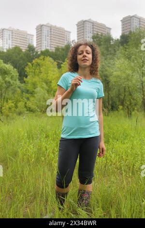 Porträt einer jungen Frau in voller Länge in einem urbanen Waldgebiet in der Nähe des Apartmentkomplexes Stockfoto
