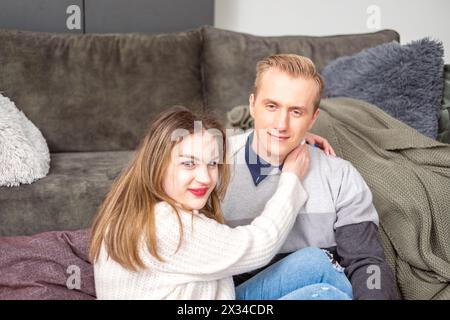 Nahaufnahme einer liebevollen Umarmung, mit einer Frau in einem weißen Pullover und einem Mann in einem grauen gestreiften Oberteil, die Wärme und Glück in einer häuslichen Umgebung vermitteln. H Stockfoto