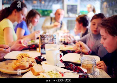 Sieben Personen sitzen am Tisch und essen im Café - Teller mit Essen und Brot stehen auf dem Tisch, konzentrieren Sie sich auf Teller Stockfoto