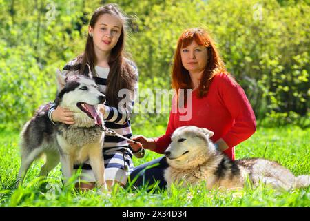 Tochter und Mutter zusammen mit zwei Hunden im Park auf dem Hintergrund grüner Bäume Stockfoto