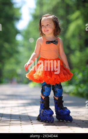 Ein kleines Mädchen im Rock mit Rollklingen und lächelt am Sommertag im Park Stockfoto