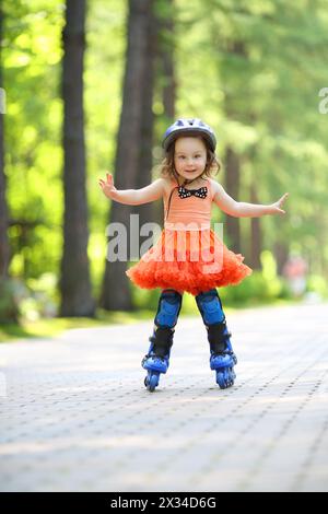 Kleines süßes Mädchen im Rock und Helm Rollschuhe im Garten am Sommertag Stockfoto