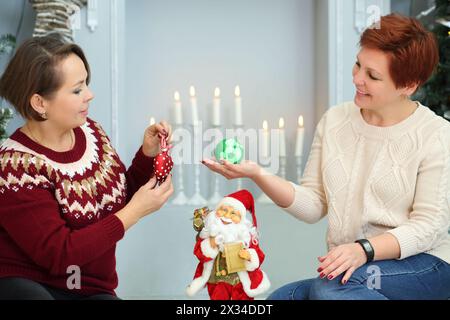 Zwei Frauen sitzen auf dem Boden mit weihnachtskugeln neben dem Kamin mit Kerzen Stockfoto