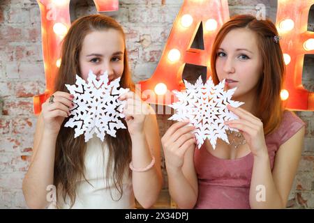 Zwei Teenager sitzen mit Papierschneeflocken neben beleuchteten Buchstaben im Studio Stockfoto