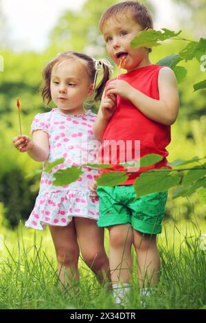 Kleine hübsche Mädchen und Junge lecken Lutscher im sonnigen grünen Park Stockfoto