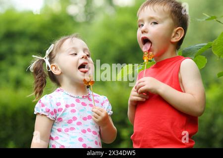 Das kleine hübsche Mädchen und der Junge lecken Lutscher im grünen Sommerpark Stockfoto