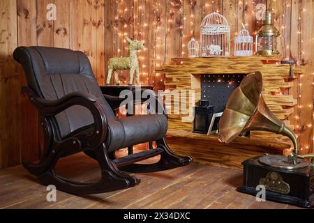 Schaukelstuhl und Grammophon in der Nähe des Kamins im Zimmer mit Holzwänden und Holzboden. Stockfoto
