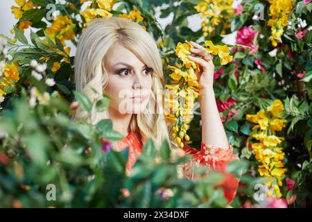 Junge blonde Frau in rotem Kleid, umgeben von Blumen. Stockfoto