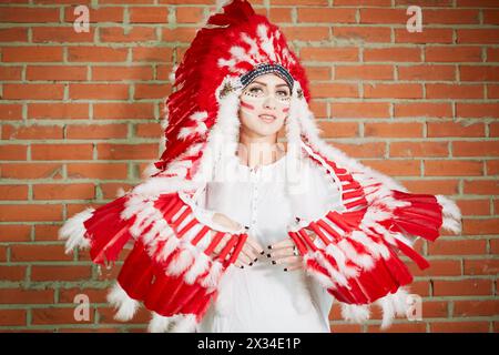 Eine junge Frau mit einem Hut aus Federn und Armen, die mit Federn wie Flügeln bedeckt sind. Stockfoto