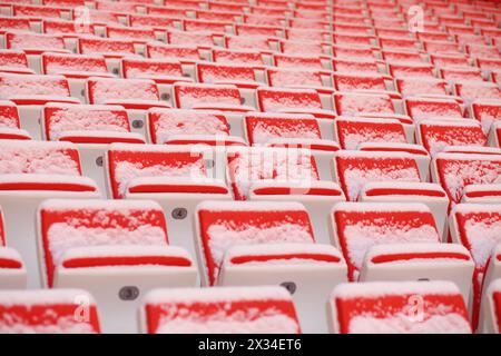 Reihen von hellen, leeren Sitzplätzen der Tribünen, die im Stadion von Schnee bedeckt sind Stockfoto