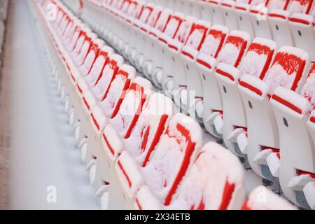 Reihen roter, leerer Sitzplätze der Tribünen, die im Stadion mit Schnee bedeckt sind Stockfoto