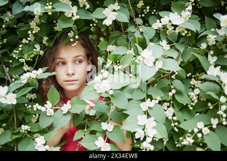 Nahaufnahme Gesicht eines kleinen Mädchens schaut aus blühendem Jasminbusch. Stockfoto