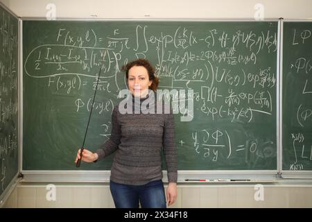 Lehrer mit Zeiger steht neben der Tafel mit mathematischen Formeln im Schulunterricht Stockfoto
