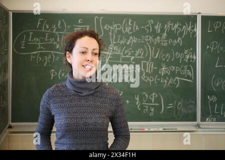 Der Lehrer spricht in der Nähe der Tafel mit mathematischen Formeln in der Schulklasse Stockfoto