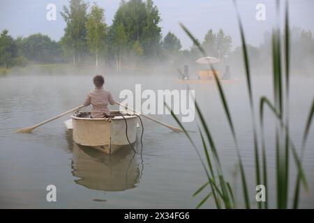 Junge Frau im Boot am Frühsommermorgen, die den Fluss hinunter zur Küste schwimmt Stockfoto