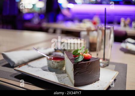 Ein Stück Kuchentaubenmilch, dekoriert mit Erdbeere und Minze auf Teller am Tisch im Café. Stockfoto