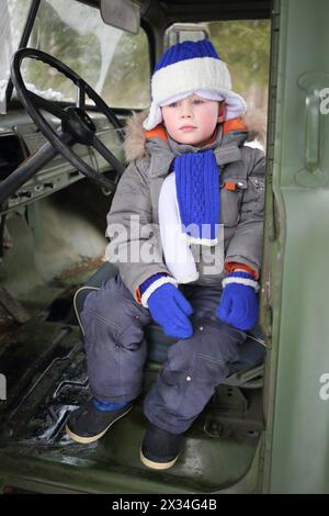 Porträt eines kleinen Jungen in Winterkleidung, der in der Kabine der alten Maschine sitzt Stockfoto