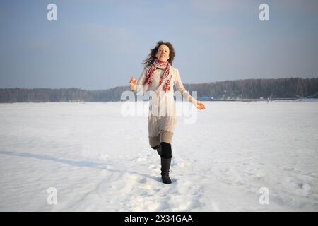 Schöne Frau mit lockigen Haaren in einem beigefarbenen Kleid, die im Schnee läuft Stockfoto