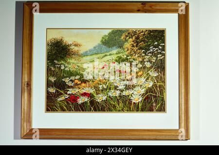 Landschaft, gestickt auf Stoff, in einem Holzrahmen an der Wand. Stockfoto